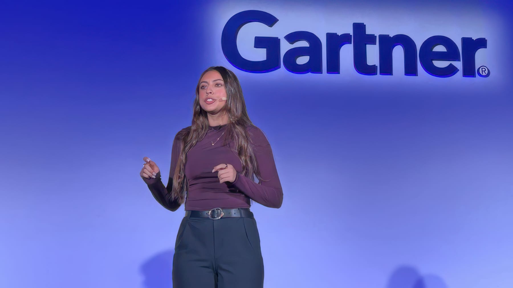 Presenter speaking on stage beneath a large glowing Gartner logo on a blue-lit wall.